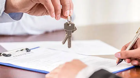 A person holding keys over papers on top of a table.