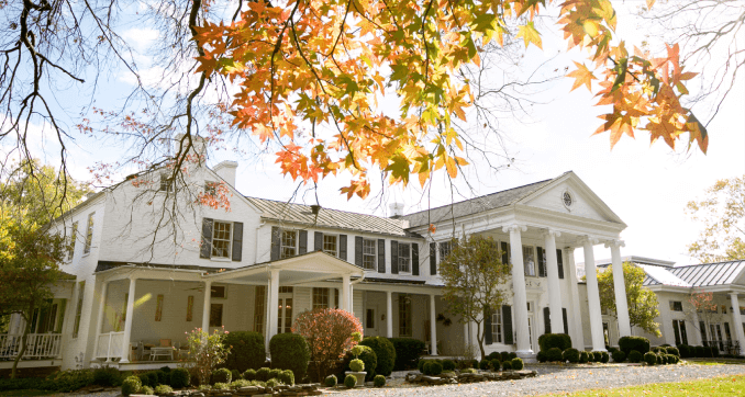 A large white house with autumn leaves on the trees.